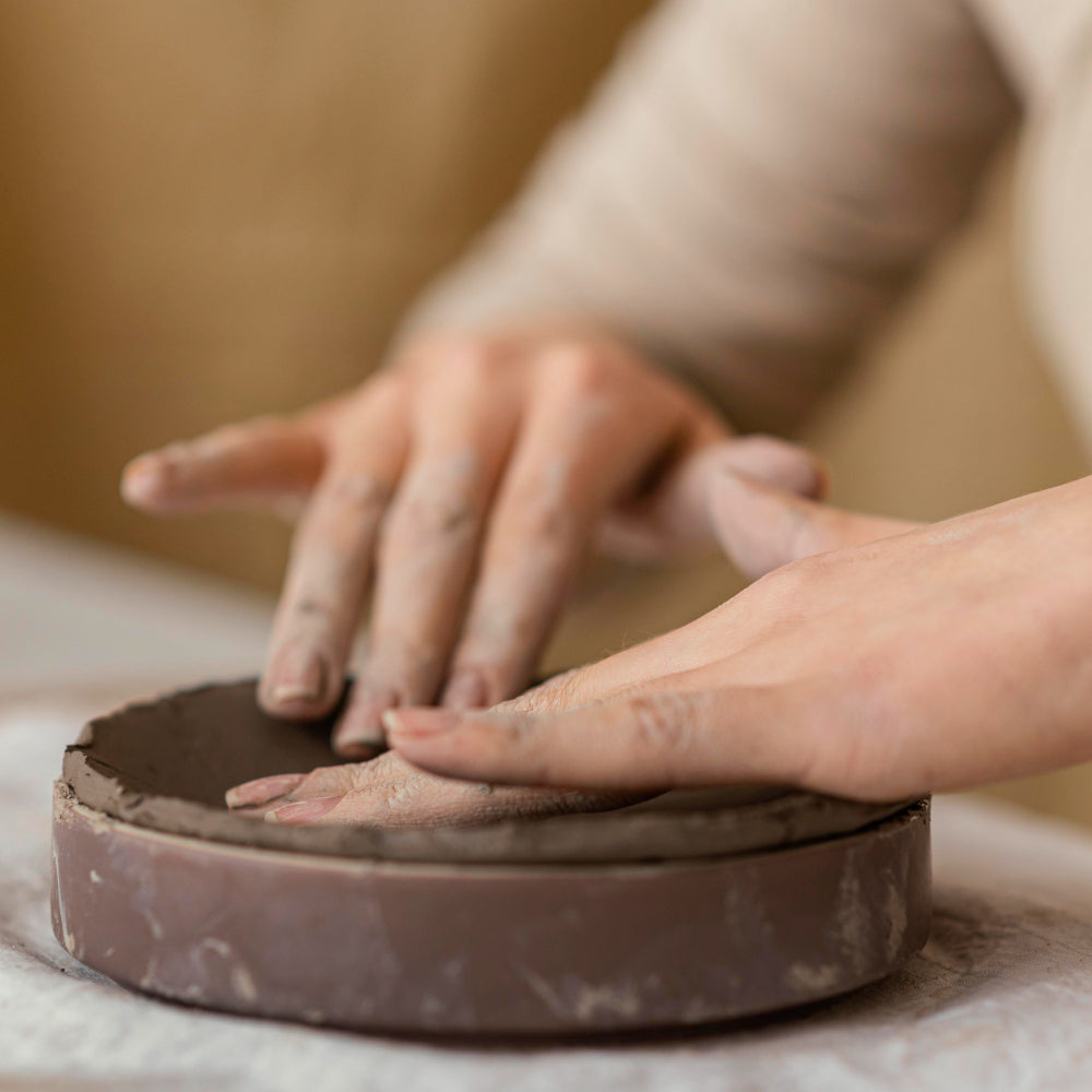 Image of a person laying clay into a mold. <a href="https://www.freepik.com/free-photo/close-up-hands-touching-clay_12812471.htm#fromView=image_search_similar&page=1&position=0&uuid=e57a6d72-2c23-4642-bf89-72e81123e553">Image by freepik</a>